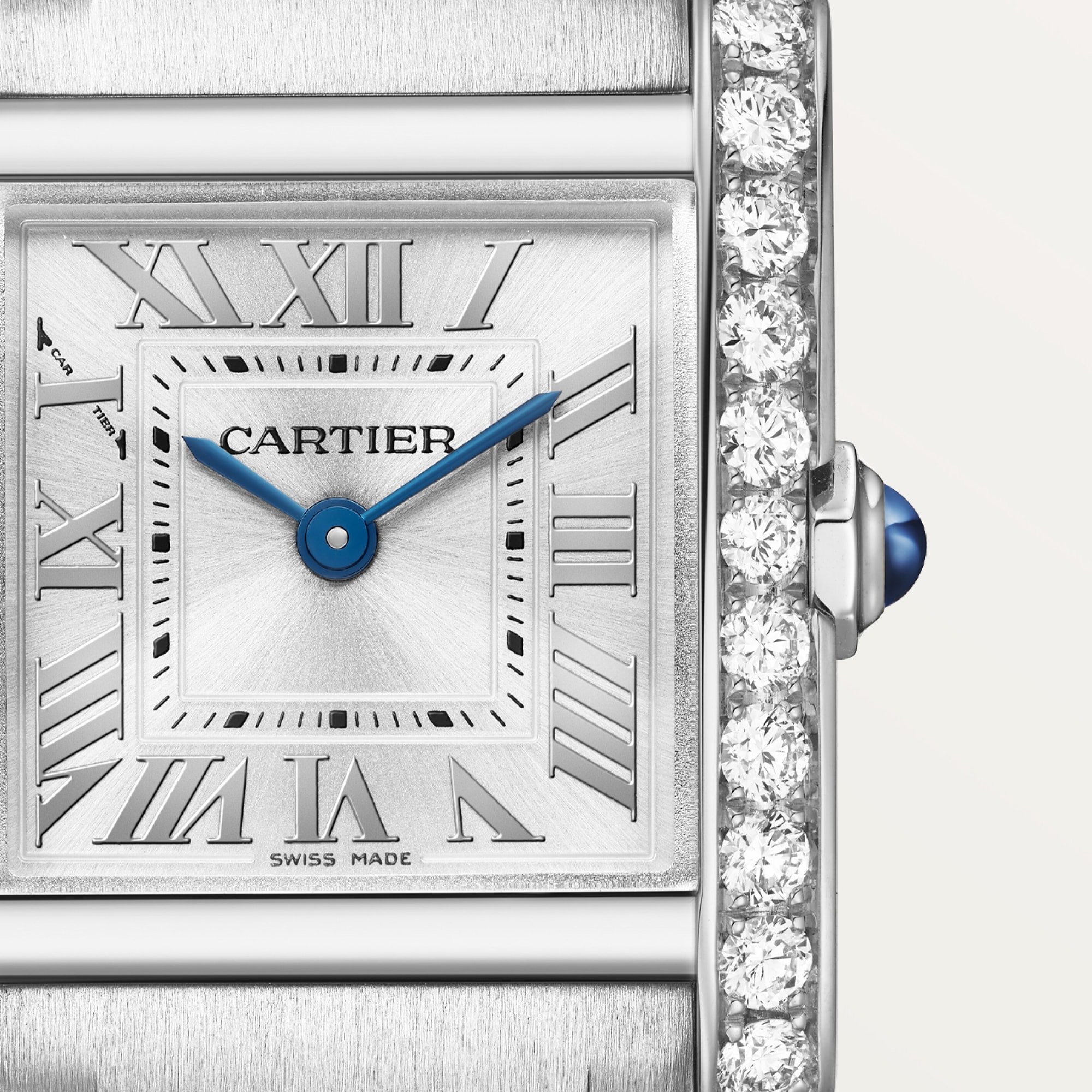 Macro shot of the dial of a Dupe Tank Française small model watch, clearly showing blue sword-shaped hands, Roman numeral markers, and brilliant diamonds on the case edge.