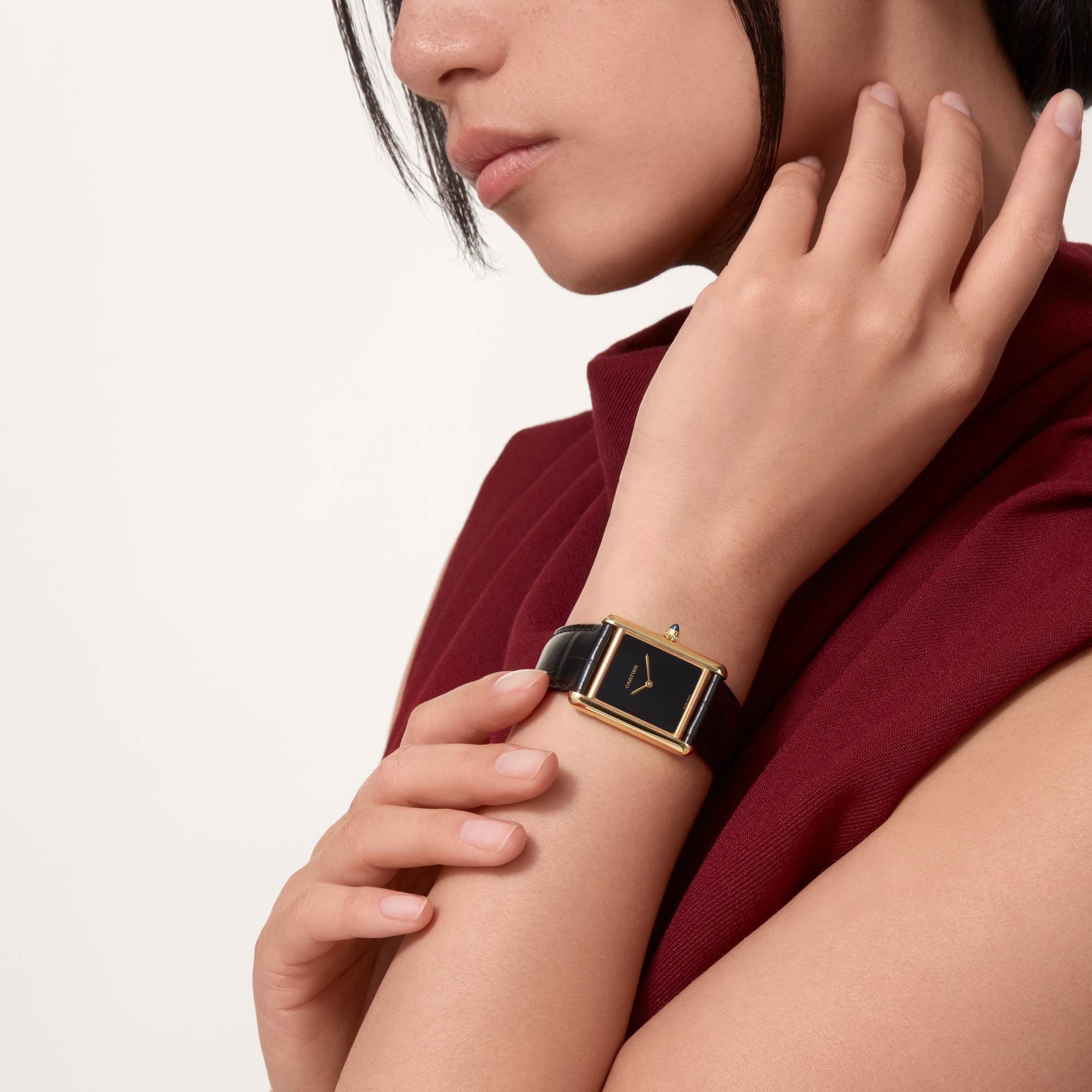 Elegant on-wrist shot of a Dupe Tank Louis Cartier large model yellow gold color watch with a black dial and black leather strap, worn by a female model.