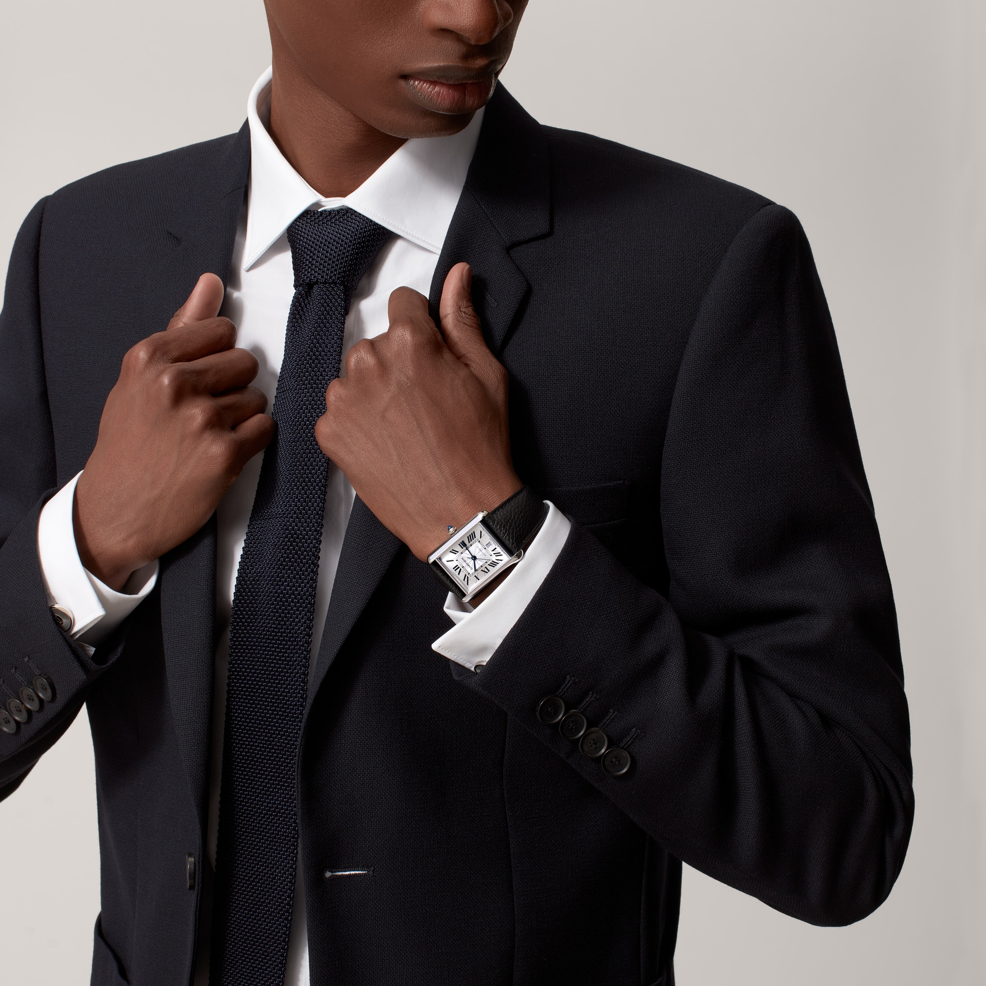 On wrist (formal): Stylish Dupe Tank Must extra-large model watch with steel case and black leather strap, worn by a male model in formal attire.