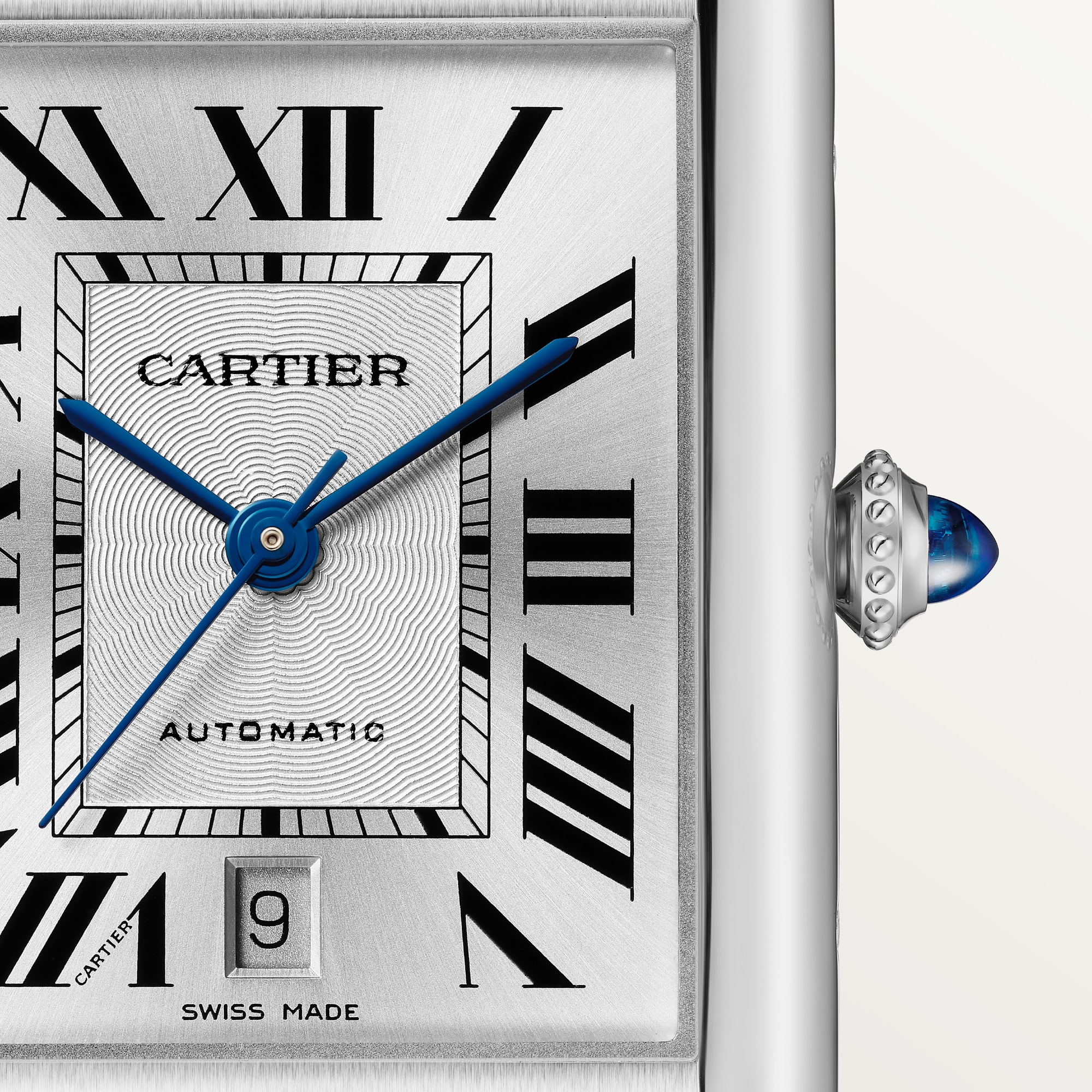 Macro shot: Dial of Dupe Tank Must extra-large model watch, steel case, with Roman numerals, blue hands, date window, and blue spinel crown.