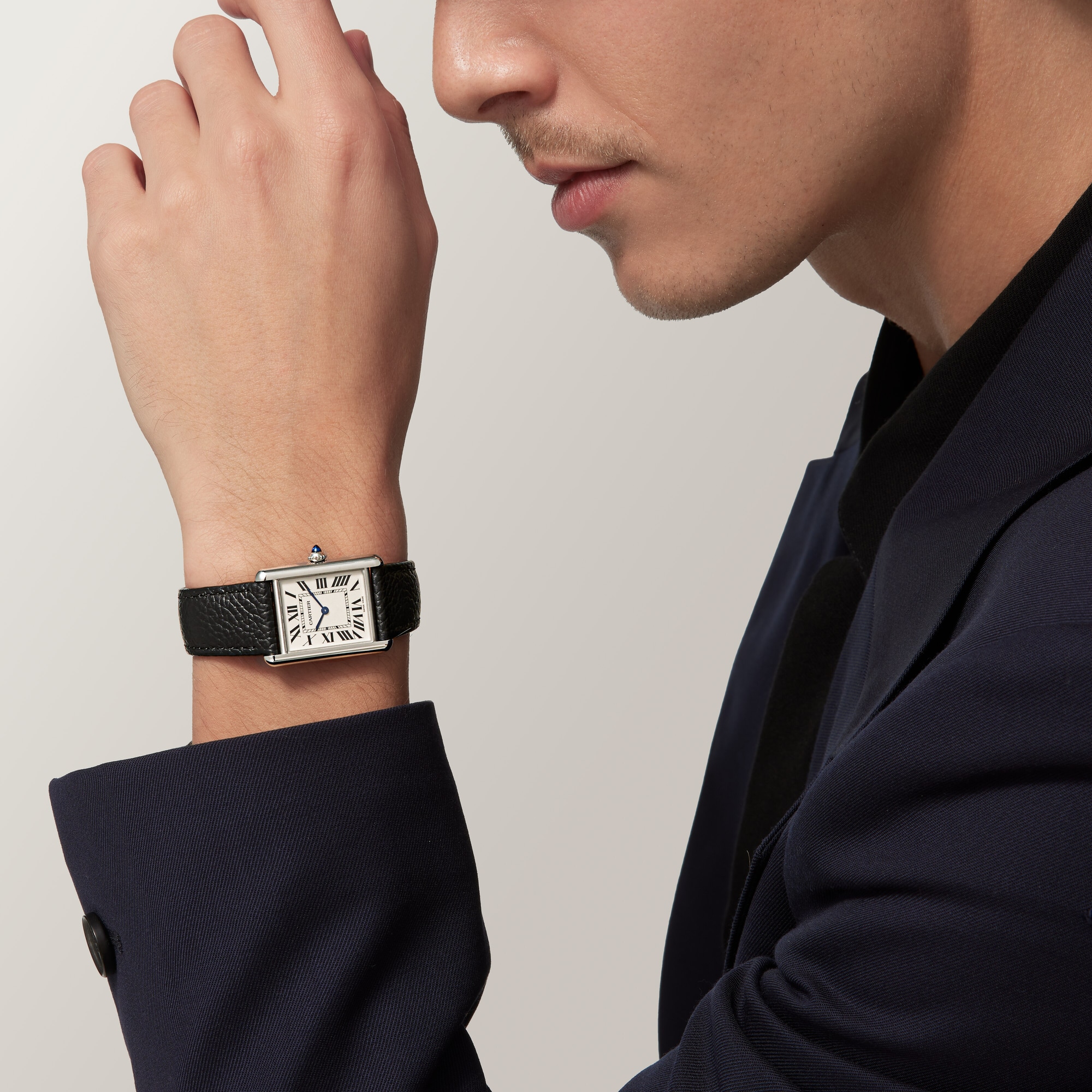 Man's wrist wearing the large steel Tank Must Solarbeat™ dupe Cartier watch with a white dial and black leather strap.