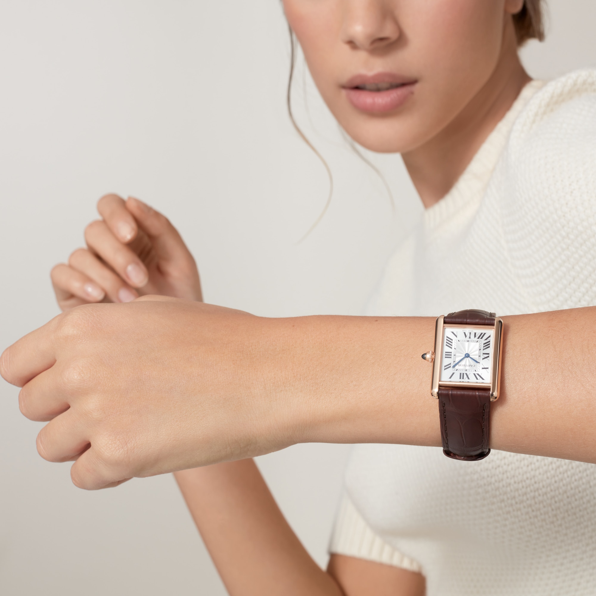 Stylish on-wrist shot of a Dupe Tank Louis Cartier large model rose gold color watch with a dark brown leather strap, worn by a female model.