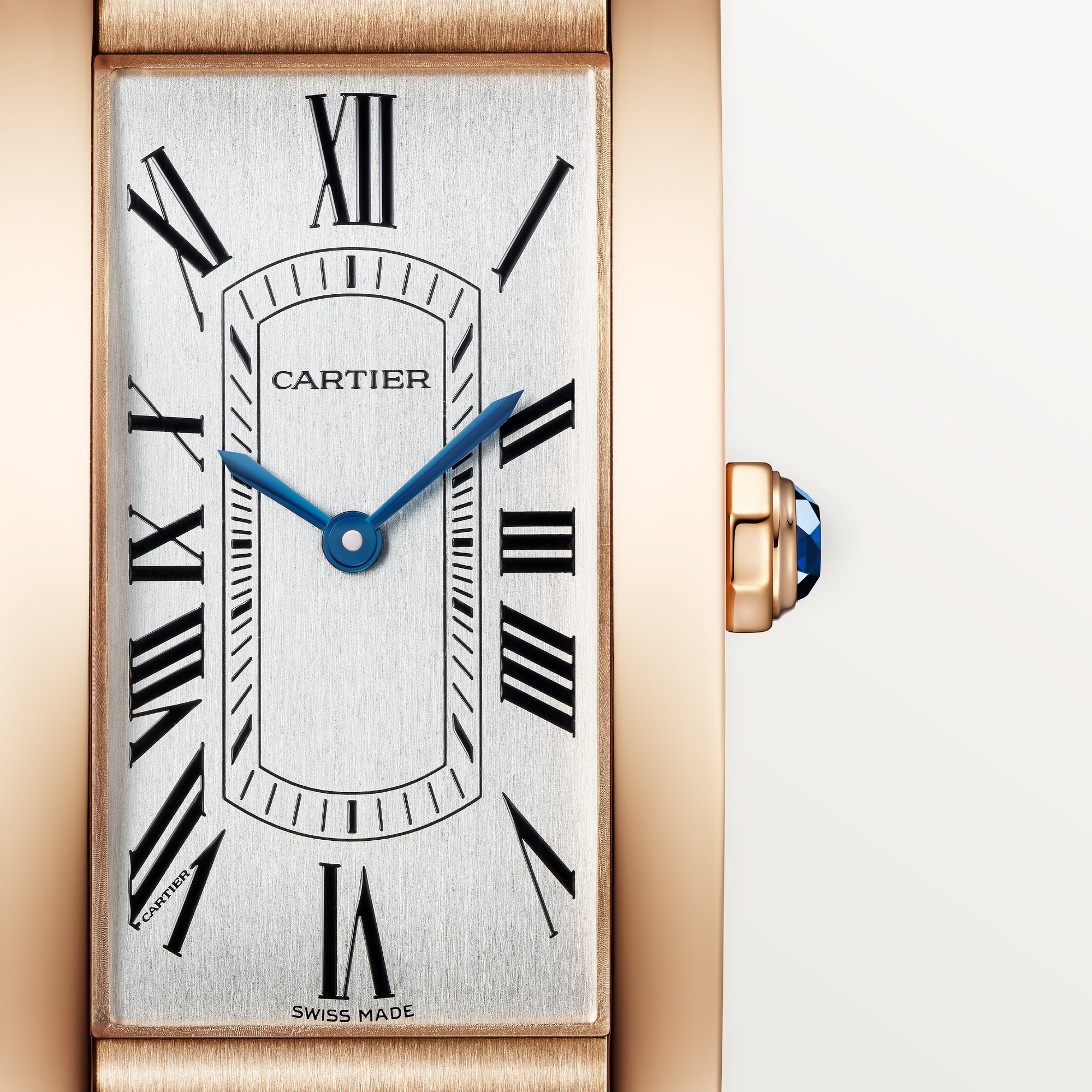 Macro shot of the dial on a Dupe Tank Américaine large model watch with a rose gold colors case, showing Roman numerals, blue hands, and the crown.