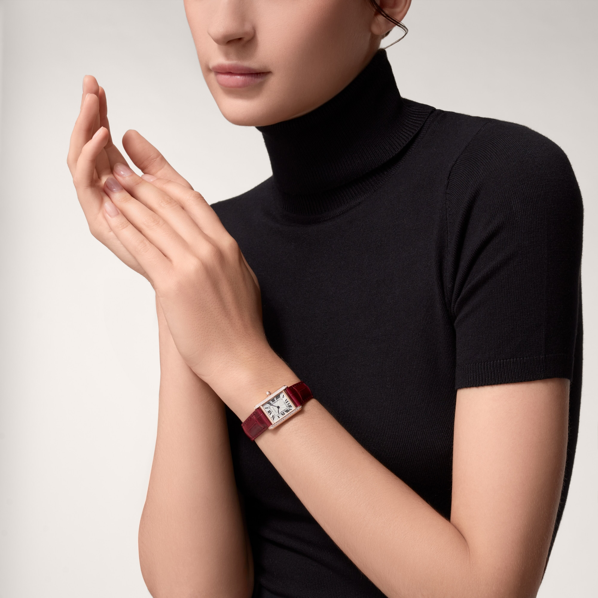 On wrist: Elegant Dupe Tank Louis Cartier small model rose gold diamond watch with burgundy leather strap, worn by a female model.