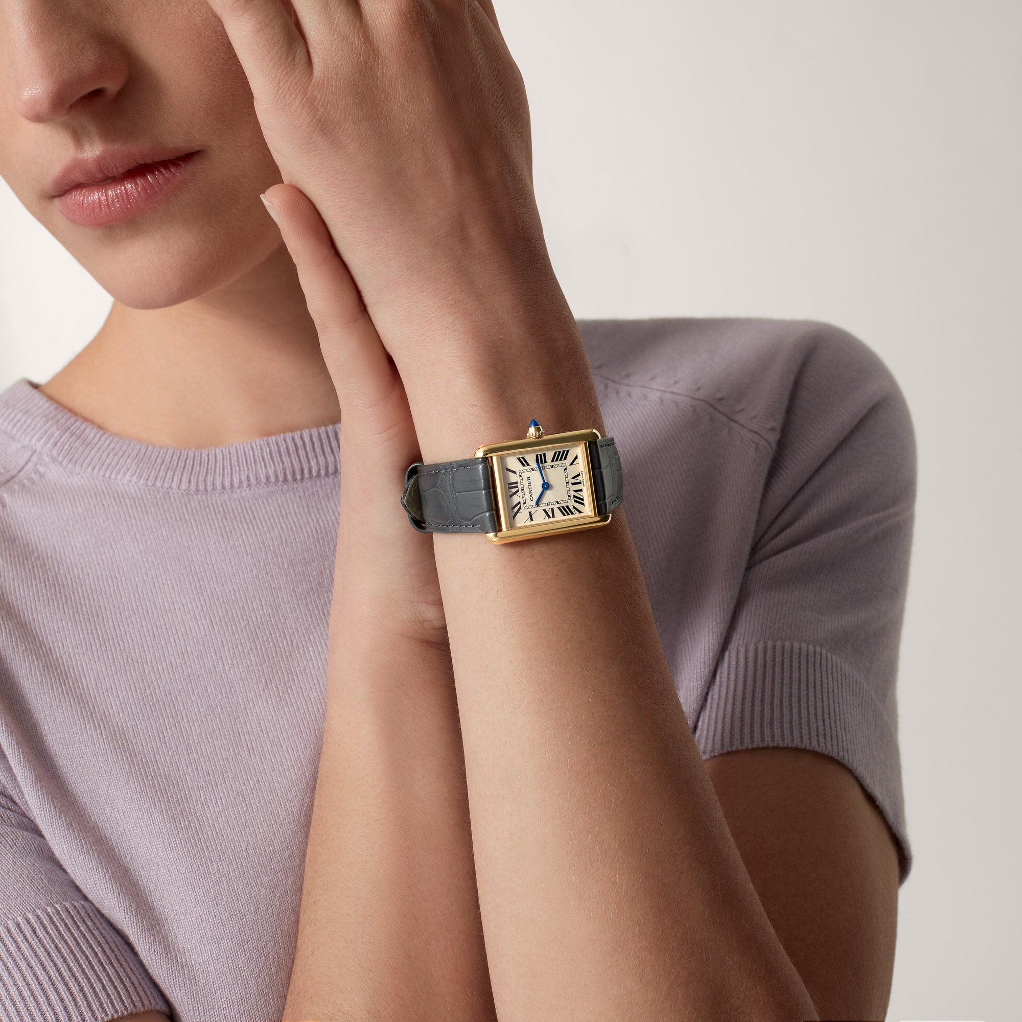 On wrist: Elegant Dupe Tank Louis Cartier large model yellow gold colors watch with black leather strap, worn by a female model.