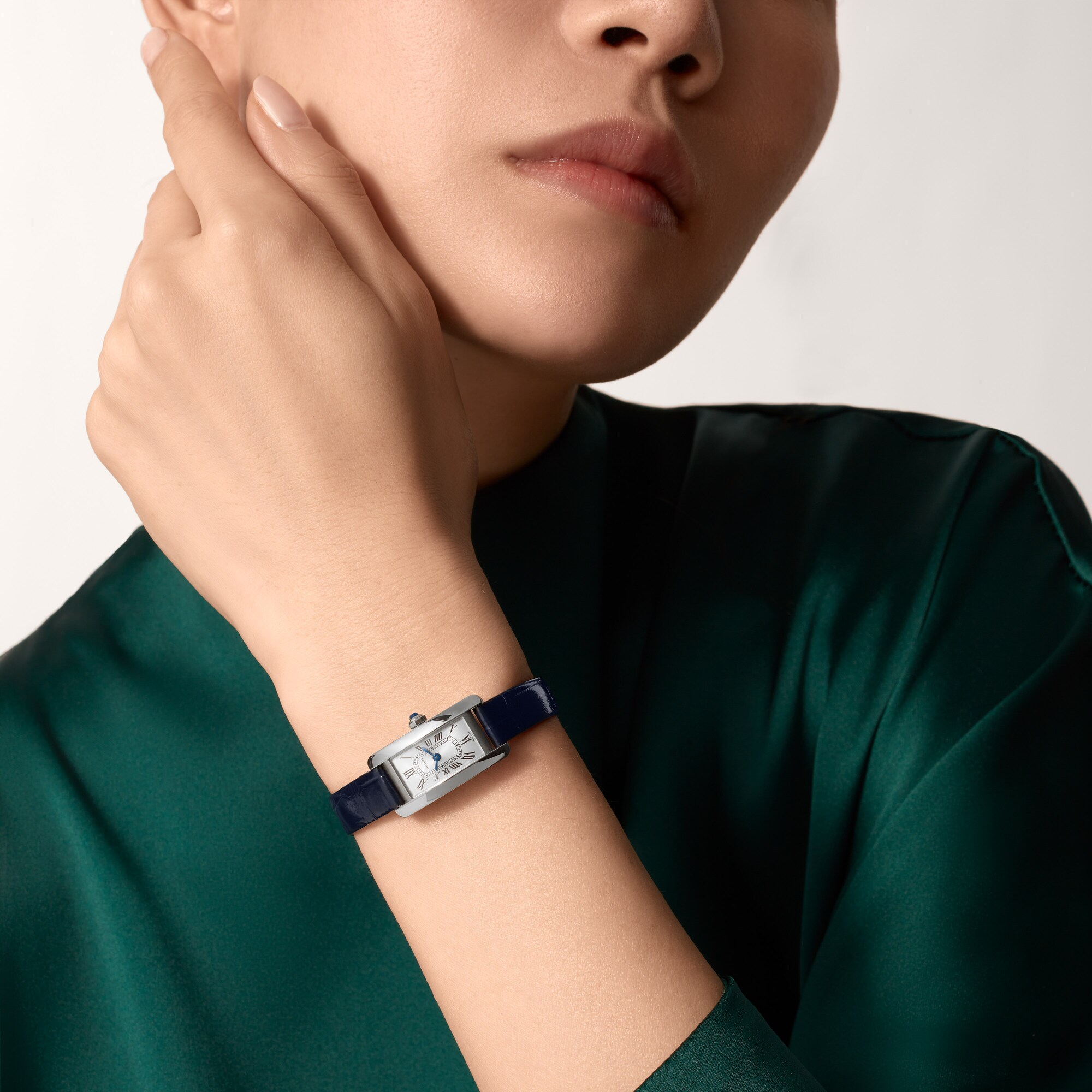 Woman's wrist showcasing the elegant mini Tank Américaine dupe Cartier watch with a silver dial and navy blue leather strap.