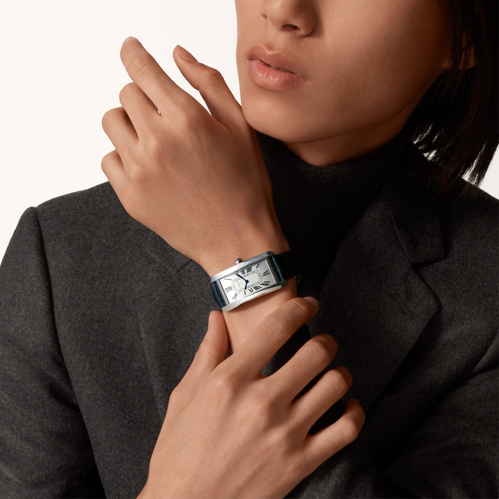 On wrist (male): Stylish Dupe Tank Américaine large model steel watch with blue leather strap, worn by a female model.