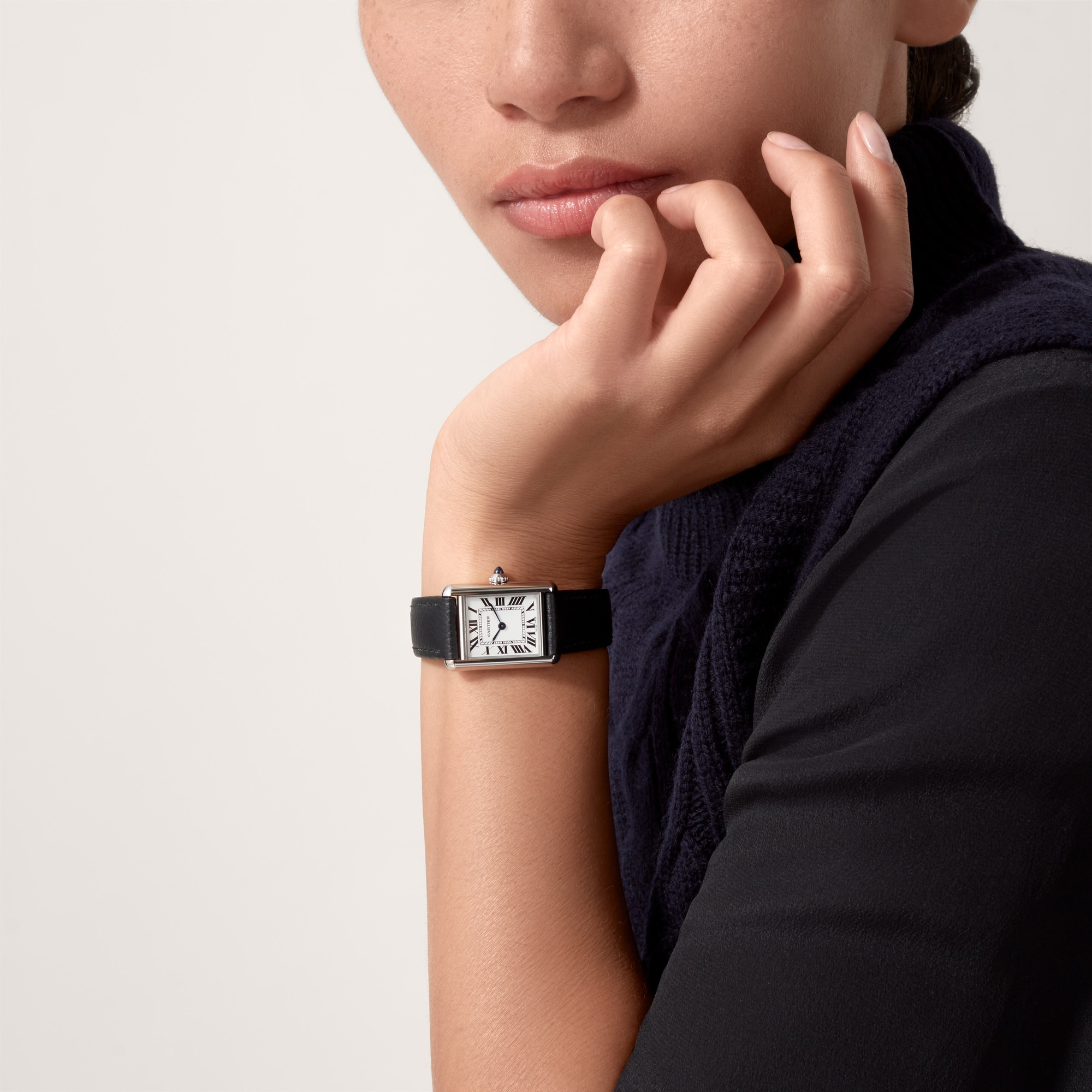 Woman's wrist elegantly showcasing the small steel Tank Must dupe Cartier watch with a white dial and black leather strap.