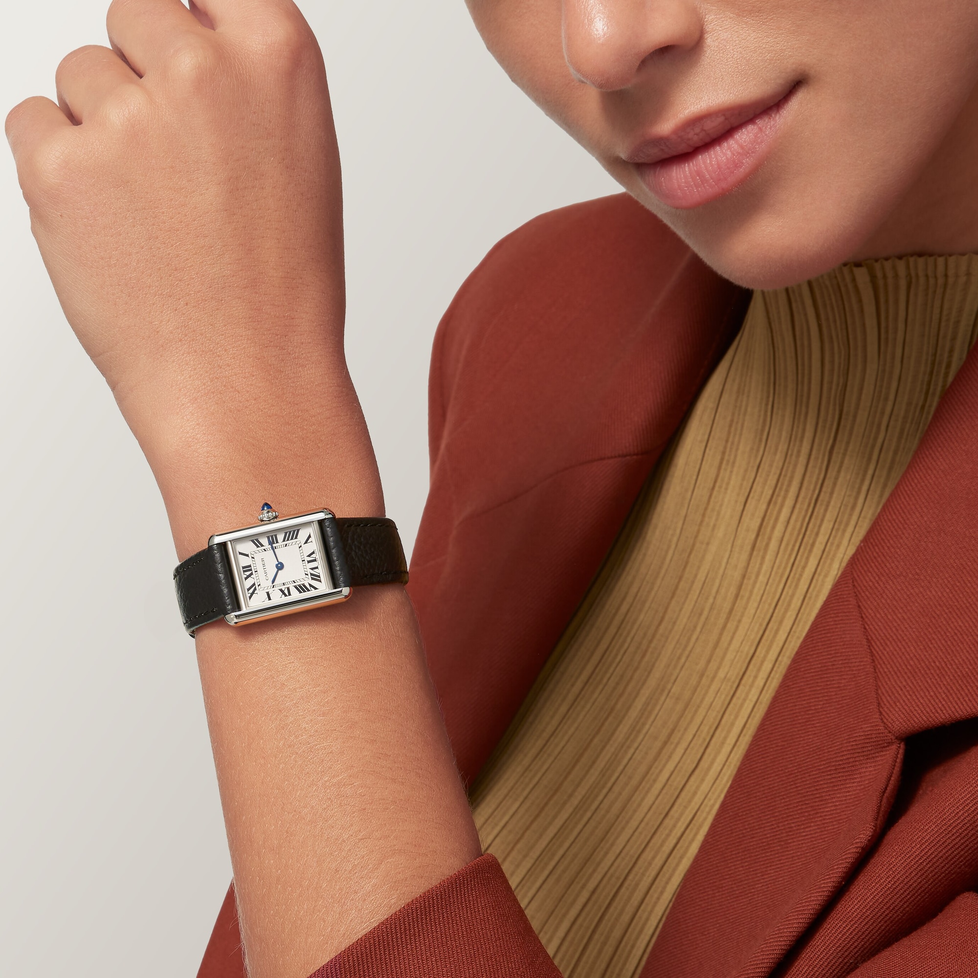 Woman's wrist showcasing the small steel Tank Must Solarbeat™ dupe Cartier watch with a white dial and black leather strap, casual style.