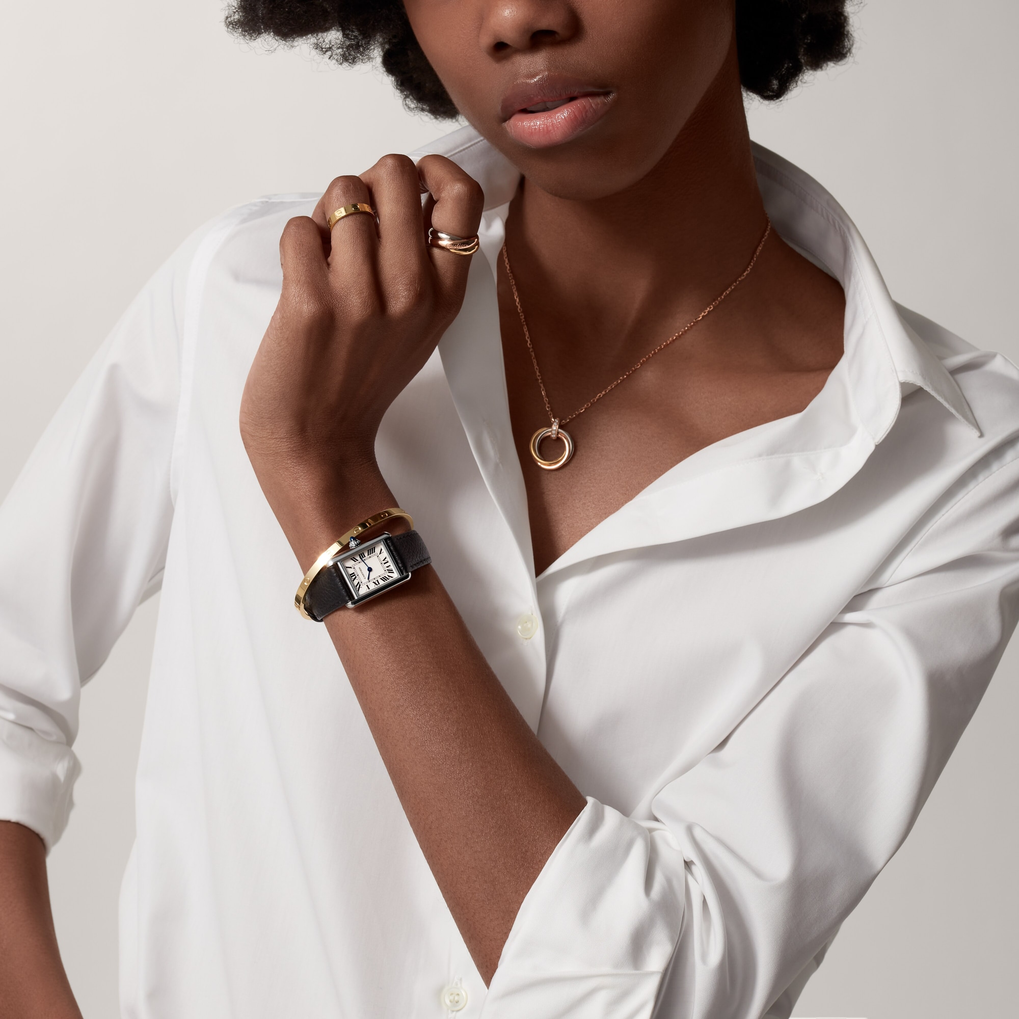 Styled shot of a woman's wrist wearing the small Tank Must dupe Cartier watch with white dial and black leather strap, paired with jewelry.