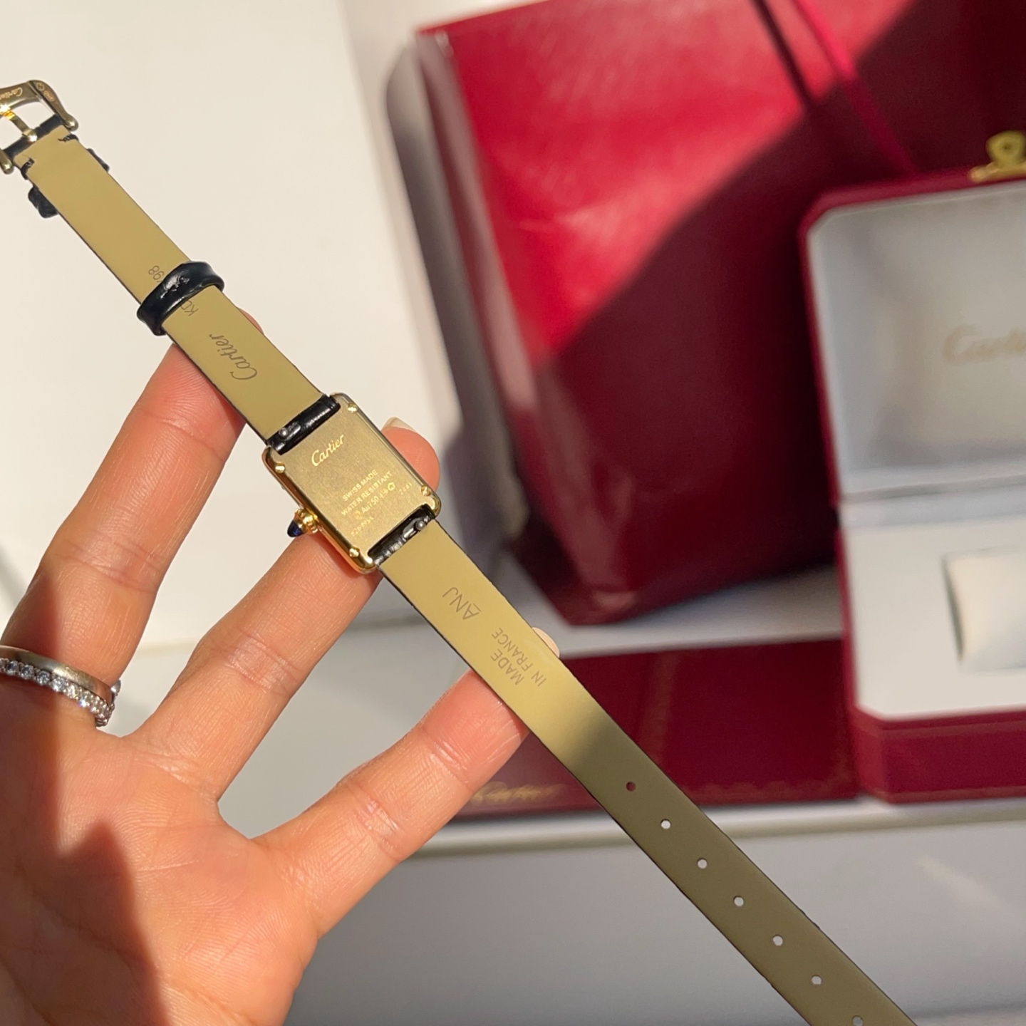 AF Super Clone Cartier Tank Louis replica watch held in hand, showing the back of the watch and its black leather strap.