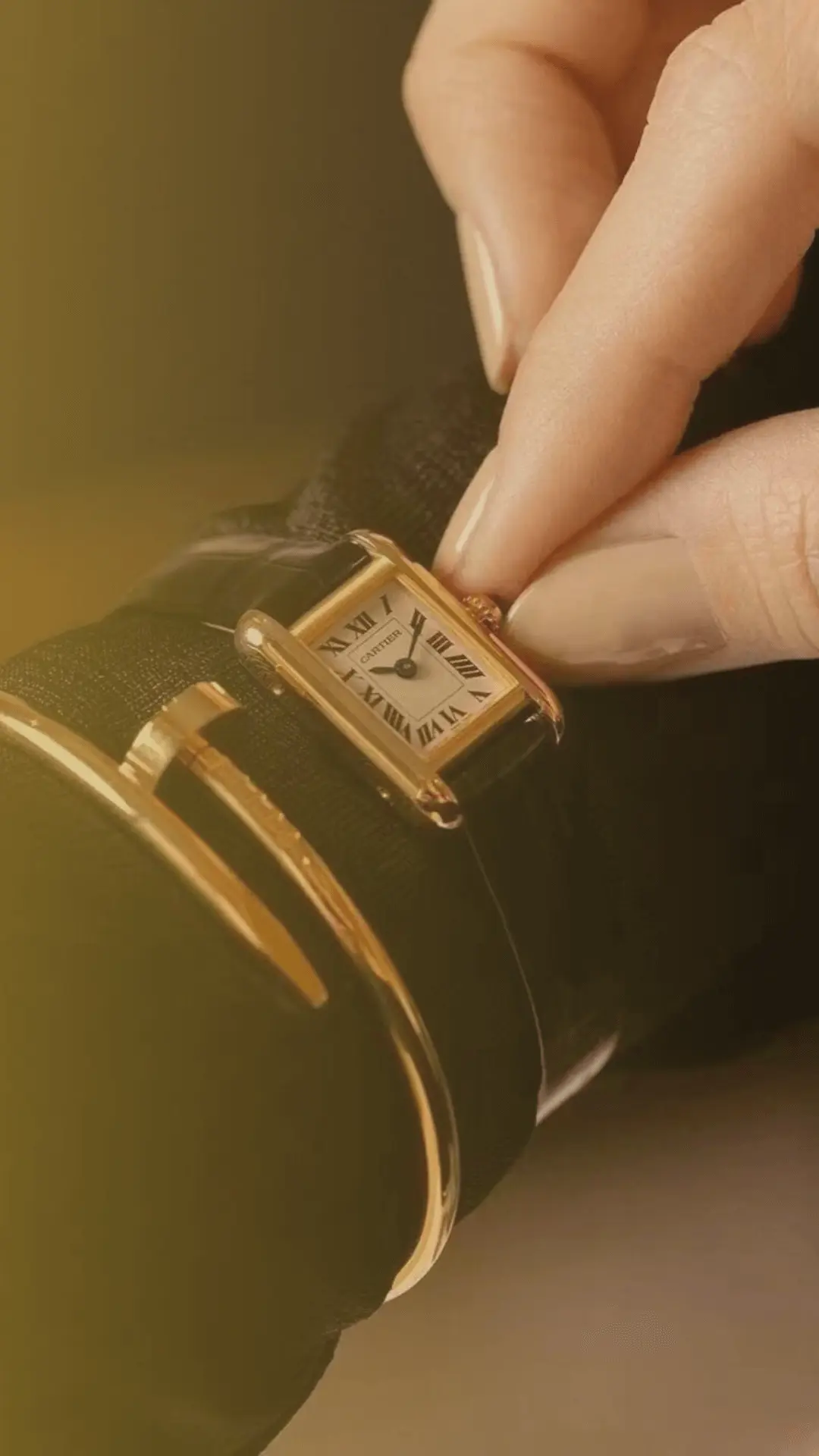 Adjusting a gold-trimmed Cartier Tank watch dupe with a dark strap, an elegant Cartier inspired watch for mobile view.