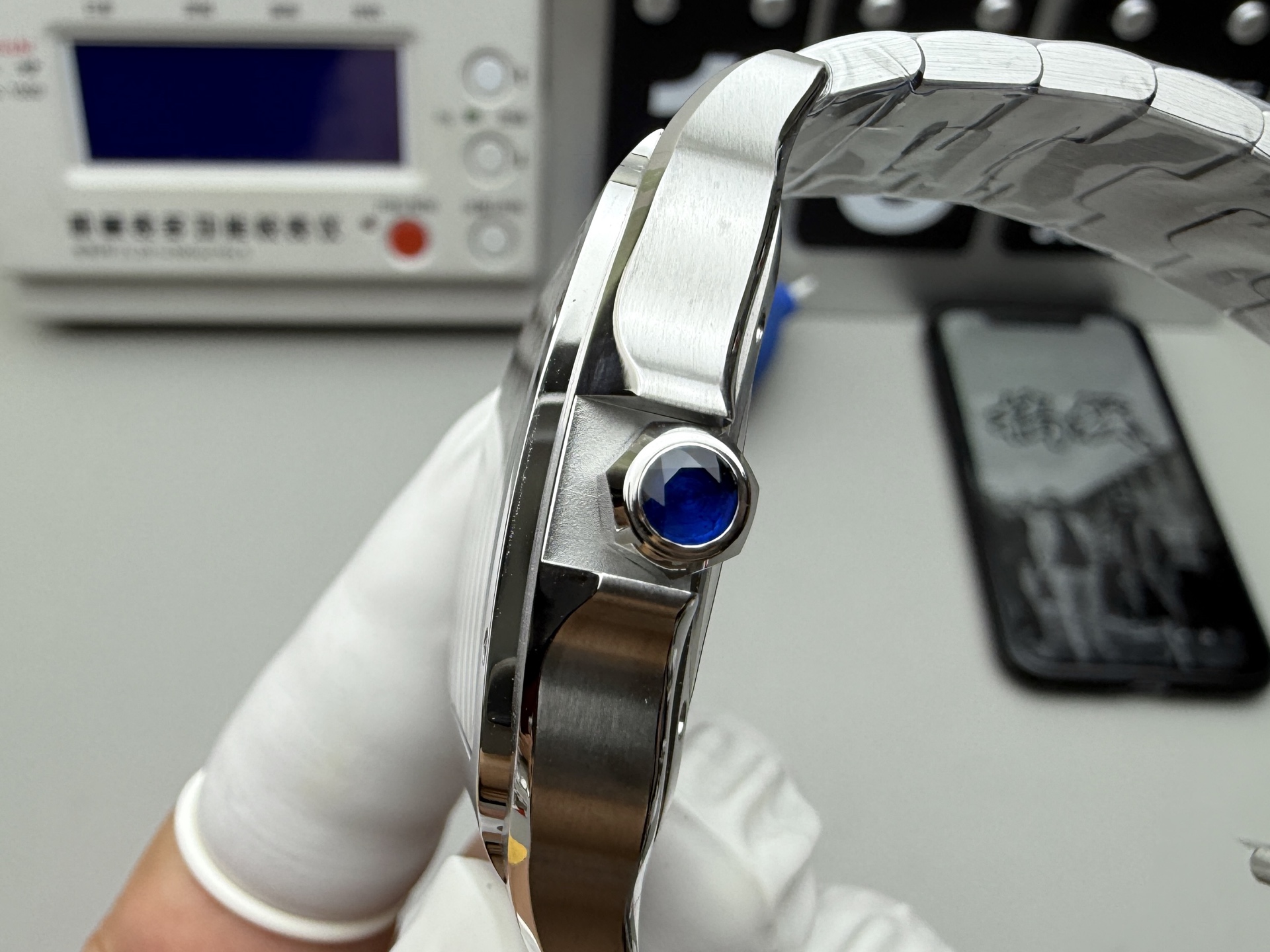 Side close-up of the crown on the BVF Super Clone Cartier Santos replica watch, featuring a blue sapphire cabochon, held by a gloved hand.