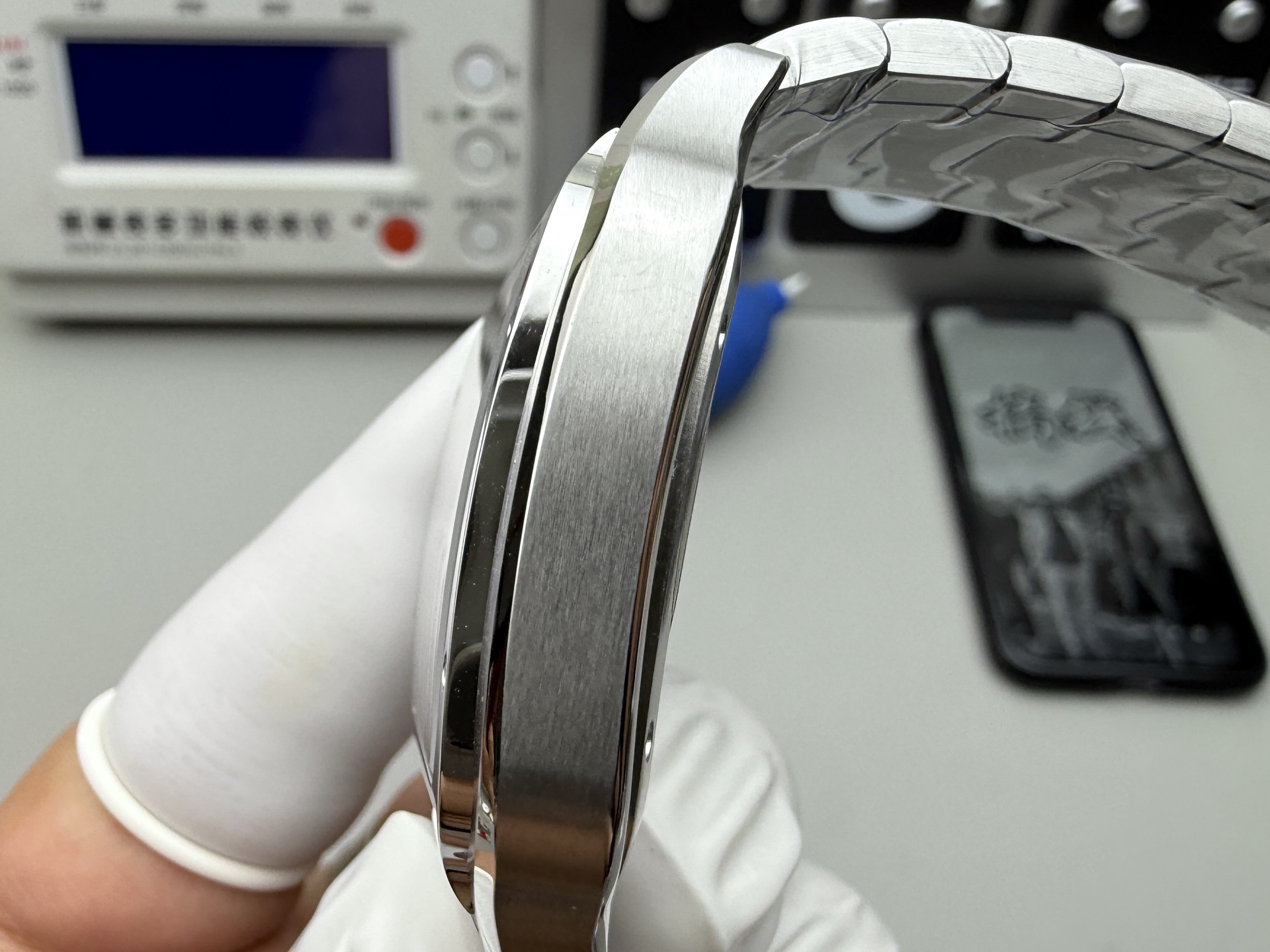 Side profile view of the BVF Super Clone Cartier Santos replica watch with a steel bracelet, held by a gloved hand, with a calendar in the background.