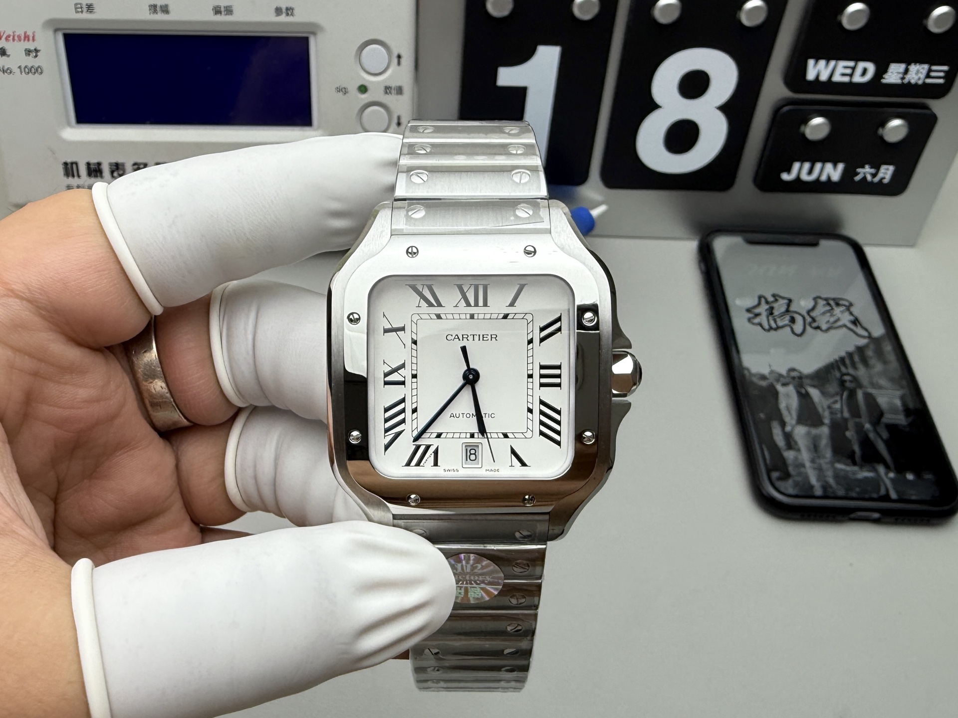 BVF Super Clone Cartier Santos replica watch with a silver case, white dial, date display, and steel bracelet, held by a gloved hand with a calendar in the background.